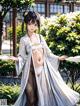 A woman in a white kimono standing in front of a tree.